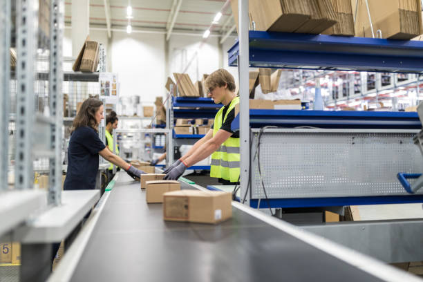 Male and female workers working on conveyor belt in a large packaging plant. Workers working in modern distribution warehouse.