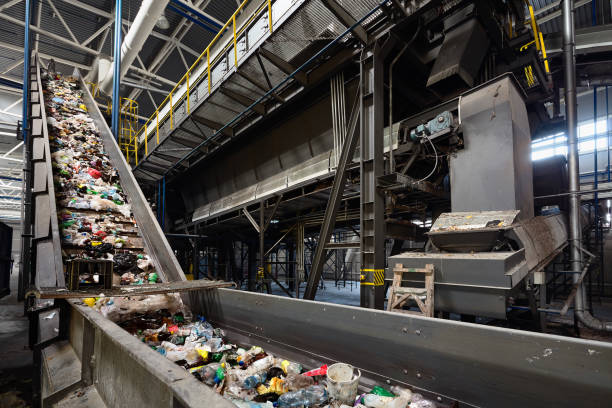 Conveyor belt at recycling plant transports garbage inside drum filter or rotating cylindrical sieve with trommel or screen for sorting pieces of garbage into various sizes fractions.