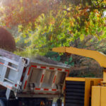 Wood chipper blowing tree branches cut a portable machine used for reducing wood into the back of a truck.