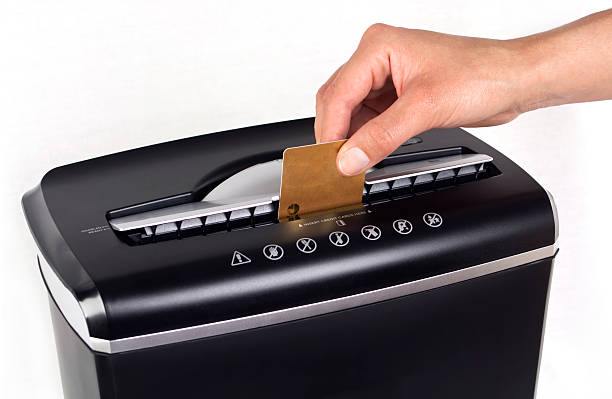 Female hand cutting or shredding a gold credit card with a black shredder isolated with copy space on white background.